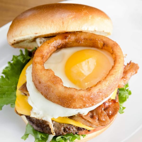 Sizzlin City Burger with a fried egg in an onion ring, cheese, bacon, and lettuce.