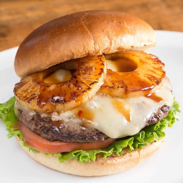 A Sizzlin City Burger with grilled pineapple, melted cheese, lettuce, and tomato on a bun.