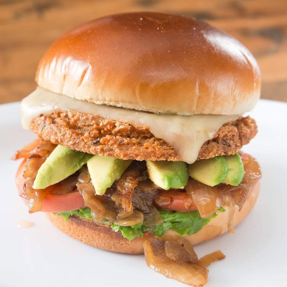 A Sizzlin City Burger with a crispy patty, melted cheese, avocado, caramelized onions, and lettuce.