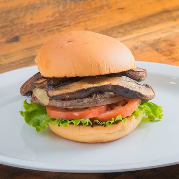 Sizzlin City Burger's mushroom and Swiss burger with lettuce, tomato, and onion on a white plate.
